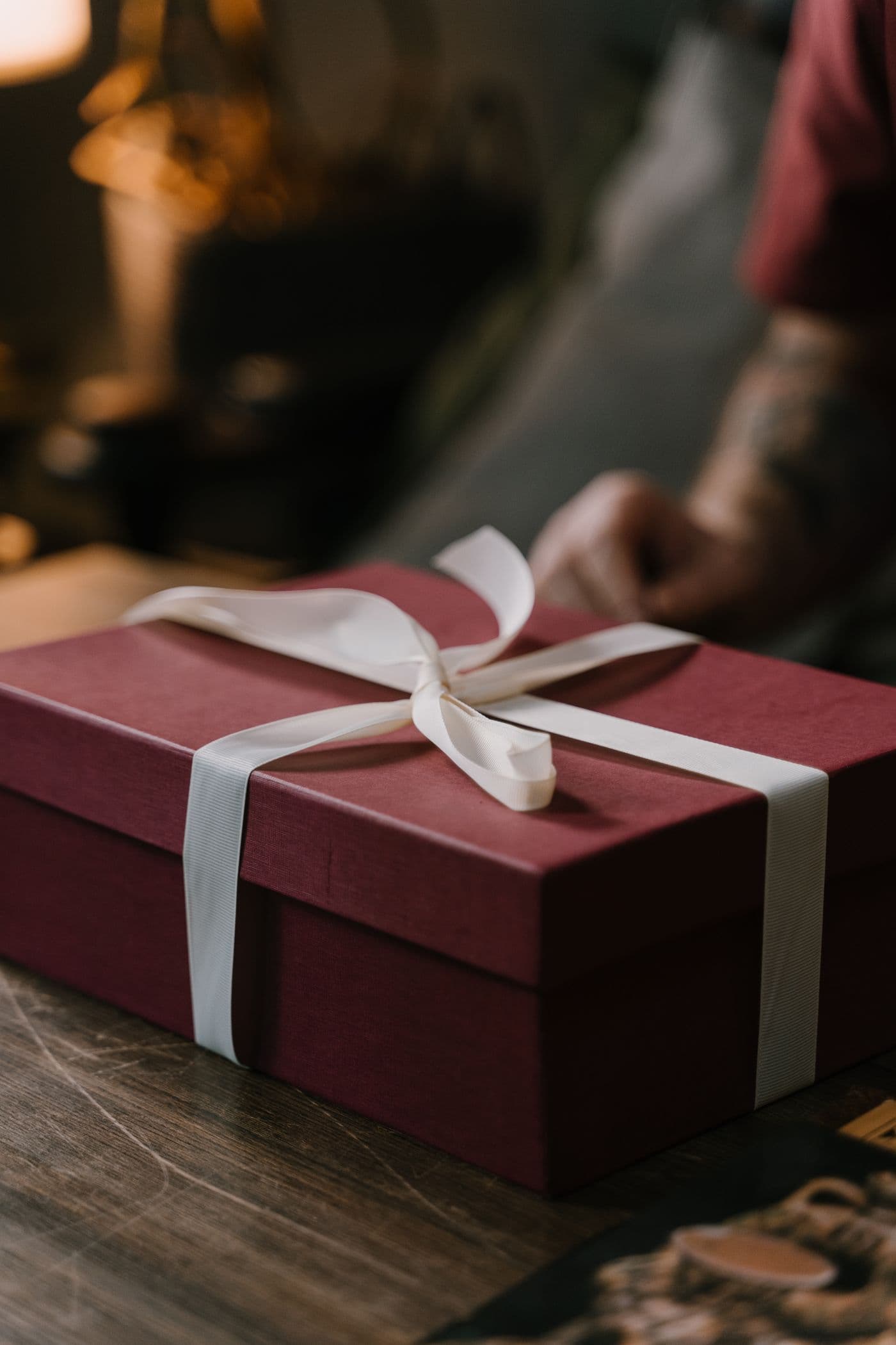 A burgundy gift box tied with a cream ribbon bow on a dark wood counter